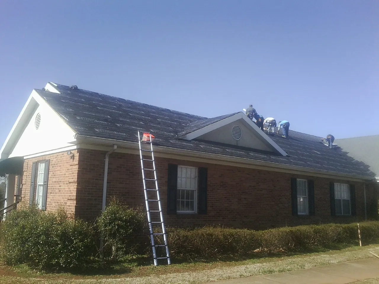 Crew tearing shingles off a brick ranch roof with a ladder set — Metal Roof Repair work by our crew in Congerville