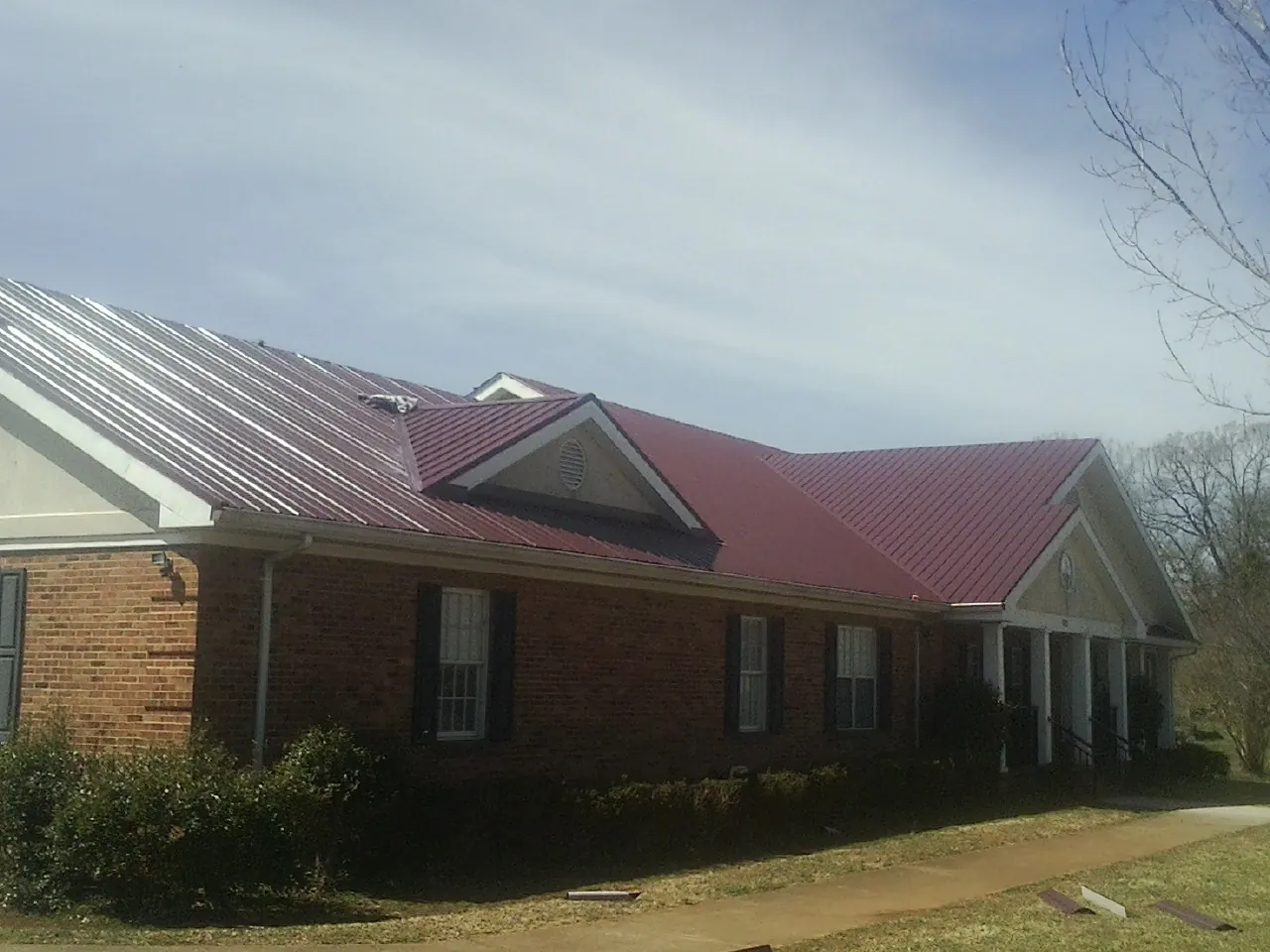 Red metal roof with gabled entries on a long brick building, from a Hail Damage Roof Repair job in Congerville