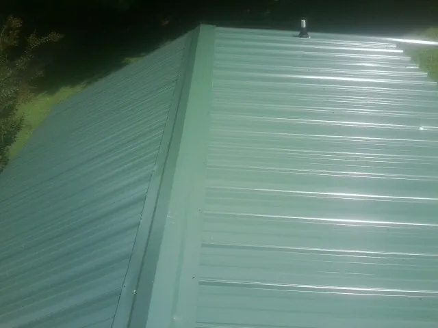 New green metal panels meeting at the ridge of a roof — Flat Roof Repair work by our crew in Congerville
