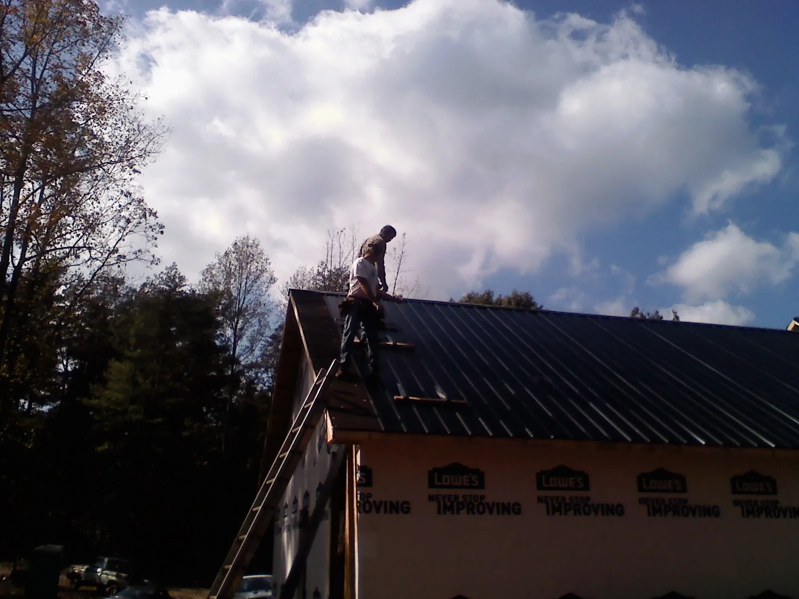 Roofer fastening dark metal panels high against a cloudy sky, from a Roof Inspection job in Congerville