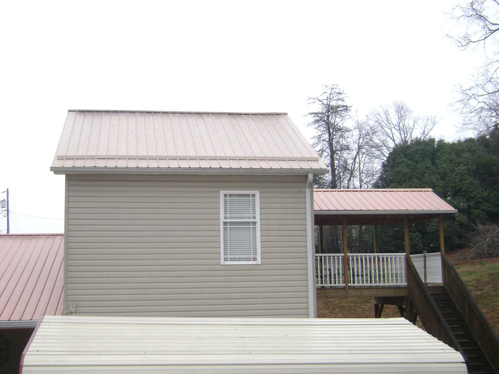 Tan metal roofs on a two story addition and attached porch, from a Roof Replacement job in Congerville